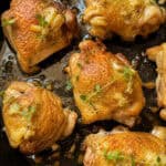 Golden-brown chicken thighs cooked in a skillet, garnished with fresh thyme sprigs and surrounded by a light garlic and herb sauce.