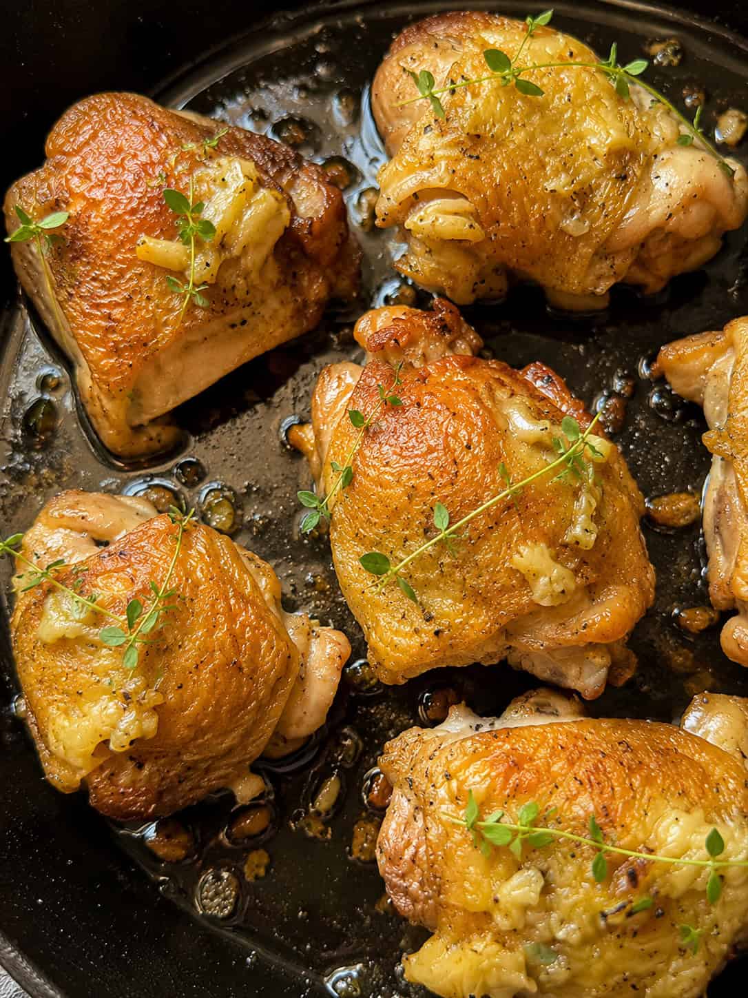 Golden-brown chicken thighs cooked in a skillet, garnished with fresh thyme sprigs and surrounded by a light garlic and herb sauce.