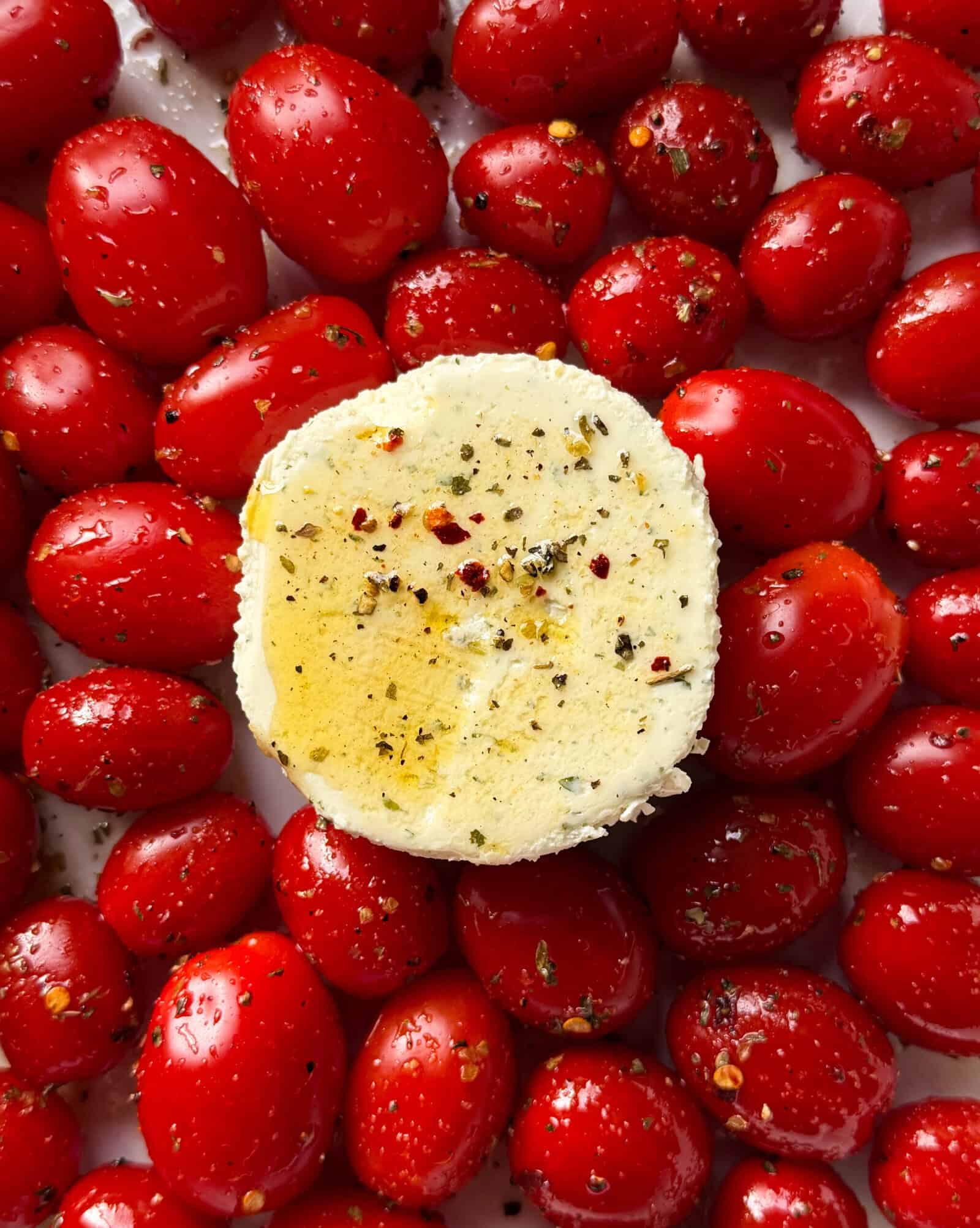 A round slice of herbed goat cheese drizzled with olive oil sits on a bed of seasoned cherry tomatoes, evoking the flavors of Creamy Boursin & Tomato Pasta.