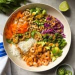A vibrant spring roll salad bowl filled with rice noodles, vermicelli noodle salad, carrots, cucumber, red cabbage, cilantro, jalapeños, avocado, peanuts, and peanut sauce. A lime wedge and fresh mint sit beside the bowl.
