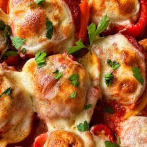 Stuffed bell peppers topped with melted, browned cheese and garnished with fresh parsley. The peppers are filled and baked, creating a golden, bubbly cheese crust.