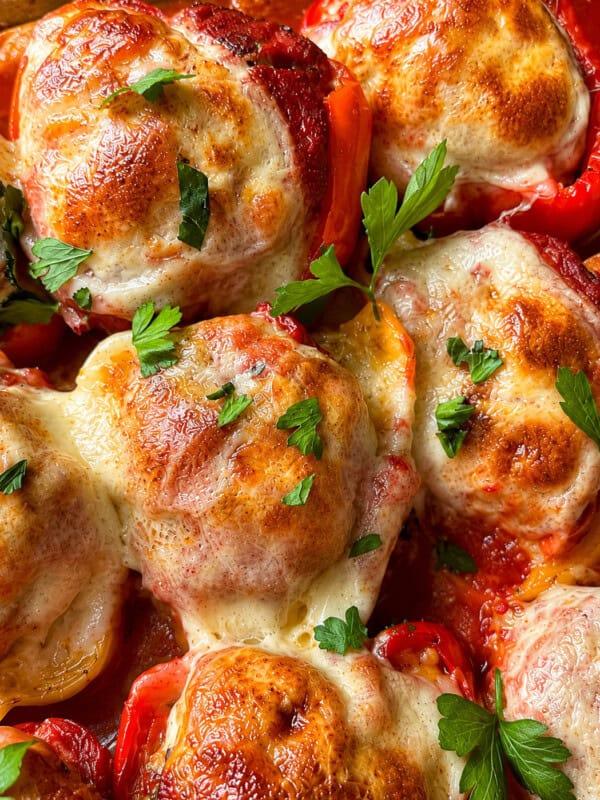 Stuffed bell peppers topped with melted, browned cheese and garnished with fresh parsley. The peppers are filled and baked, creating a golden, bubbly cheese crust.