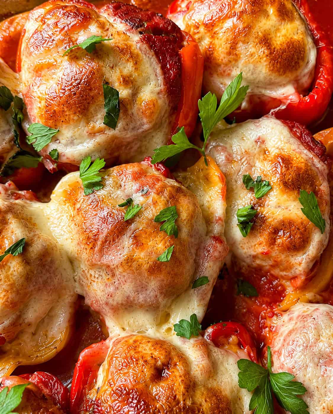 Stuffed bell peppers topped with melted, browned cheese and garnished with fresh parsley. The peppers are filled and baked, creating a golden, bubbly cheese crust.