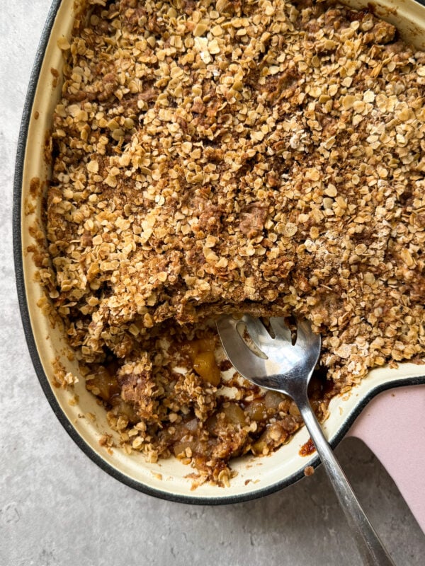 A close-up of a baked fruit crumble in a large dish, topped with a golden oat and brown sugar crust. A portion has been scooped out with a large metal spoon, revealing the fruit fillingโperfect for an Easy Apple Crisp Recipe.