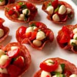 Crispy Salami Cups filled with small mozzarella balls, chopped cherry tomatoes, and fresh basil make perfect appetizers for Christmas, beautifully arranged on a white plate.