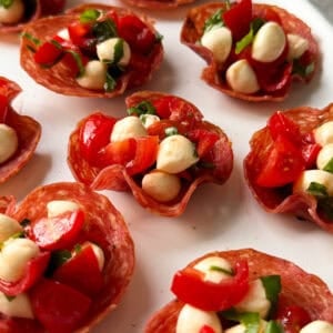 Crispy Salami Cups filled with small mozzarella balls, chopped cherry tomatoes, and fresh basil make perfect appetizers for Christmas, beautifully arranged on a white plate.