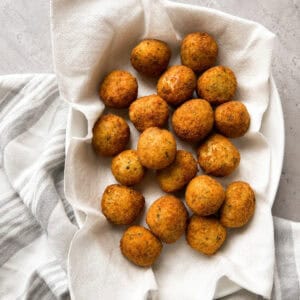 A white bowl lined with a paper towel holds golden-brown falafel balls, placed on a gray surface with a striped white and gray cloth underneath.