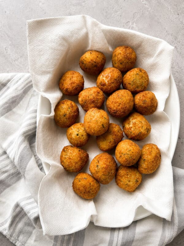 A white bowl lined with a paper towel holds golden-brown falafel balls, placed on a gray surface with a striped white and gray cloth underneath.