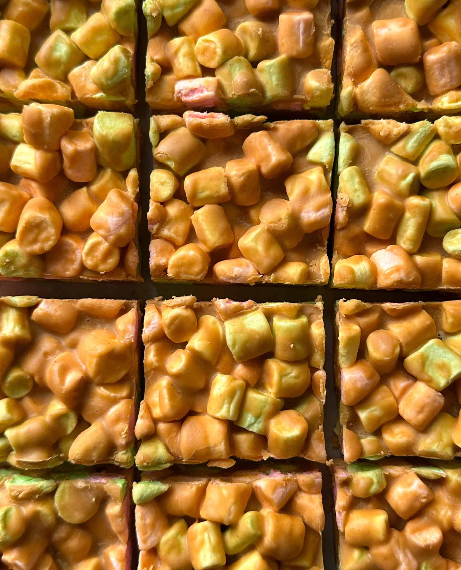 Close-up of colorful, tightly packed marshmallow squares—mostly orange and yellow with some green—in a grid pattern, resembling easy no bake desserts like peanut butter marshmallow squares cut into sweet pieces.