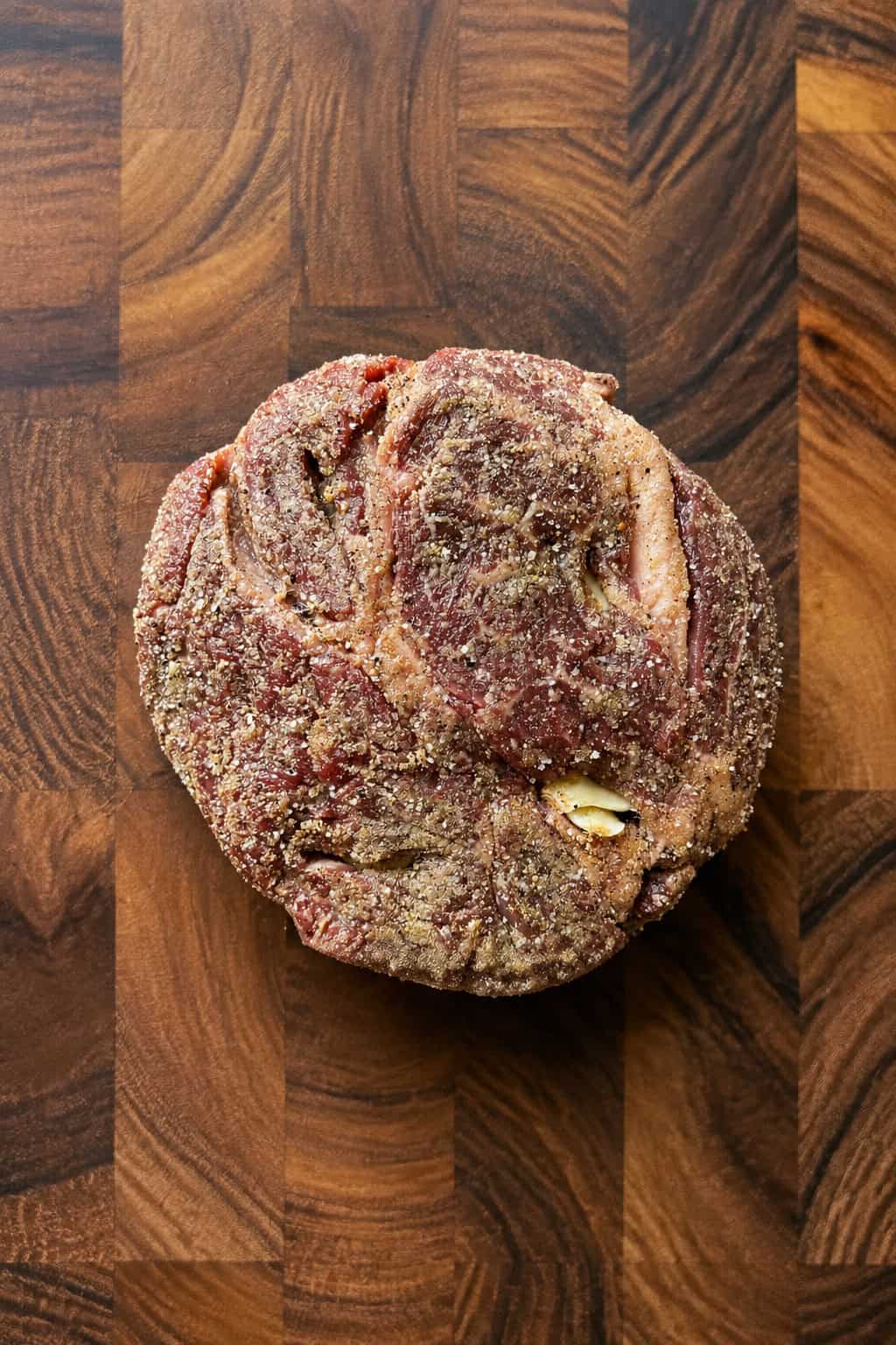 A seasoned, raw beef roast sits on a wooden cutting board, ready to be cooked.