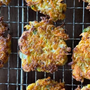 Several golden-brown cabbage fritters rest on a wire cooling rack, showing crisp, textured surfaces with visible shreds of carrot and herbs—a delicious highlight for anyone seeking an easy cabbage fritters recipe.