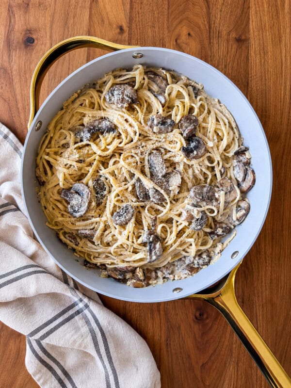 Creamy Boursin mushroom linguine in a light blue pan with gold handles, resting on a wooden surface next to a striped kitchen towel.