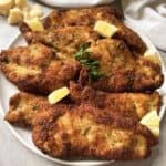 A plate of crispy, golden-brown Italian chicken cutlets garnished with fresh parsley and lemon wedges. The texture looks crunchy, and the cutlets are generously seasoned, embodying a classic Italian chicken cutlets recipe.