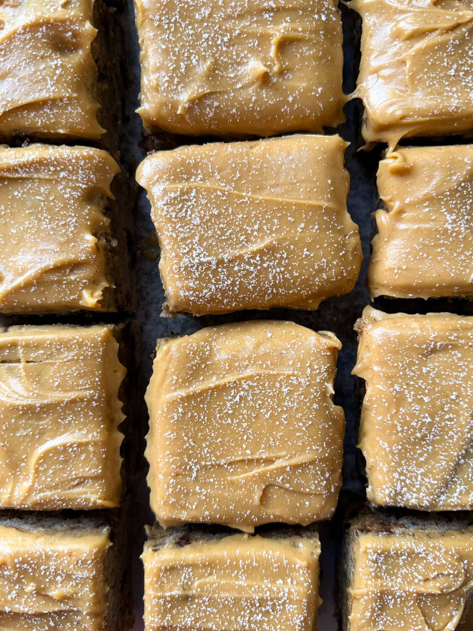 Close-up of square dessert bars topped with smooth peanut butter frosting and a sprinkling of fine white sugar, arranged in a neat grid pattern—perfect for fans of Banana Cake delights.