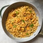 A pan filled with spaghetti tossed in a light sauce, garnished with shrimp and parsley. The pasta is evenly mixed with herbs, creating a savory and appetizing appearance.