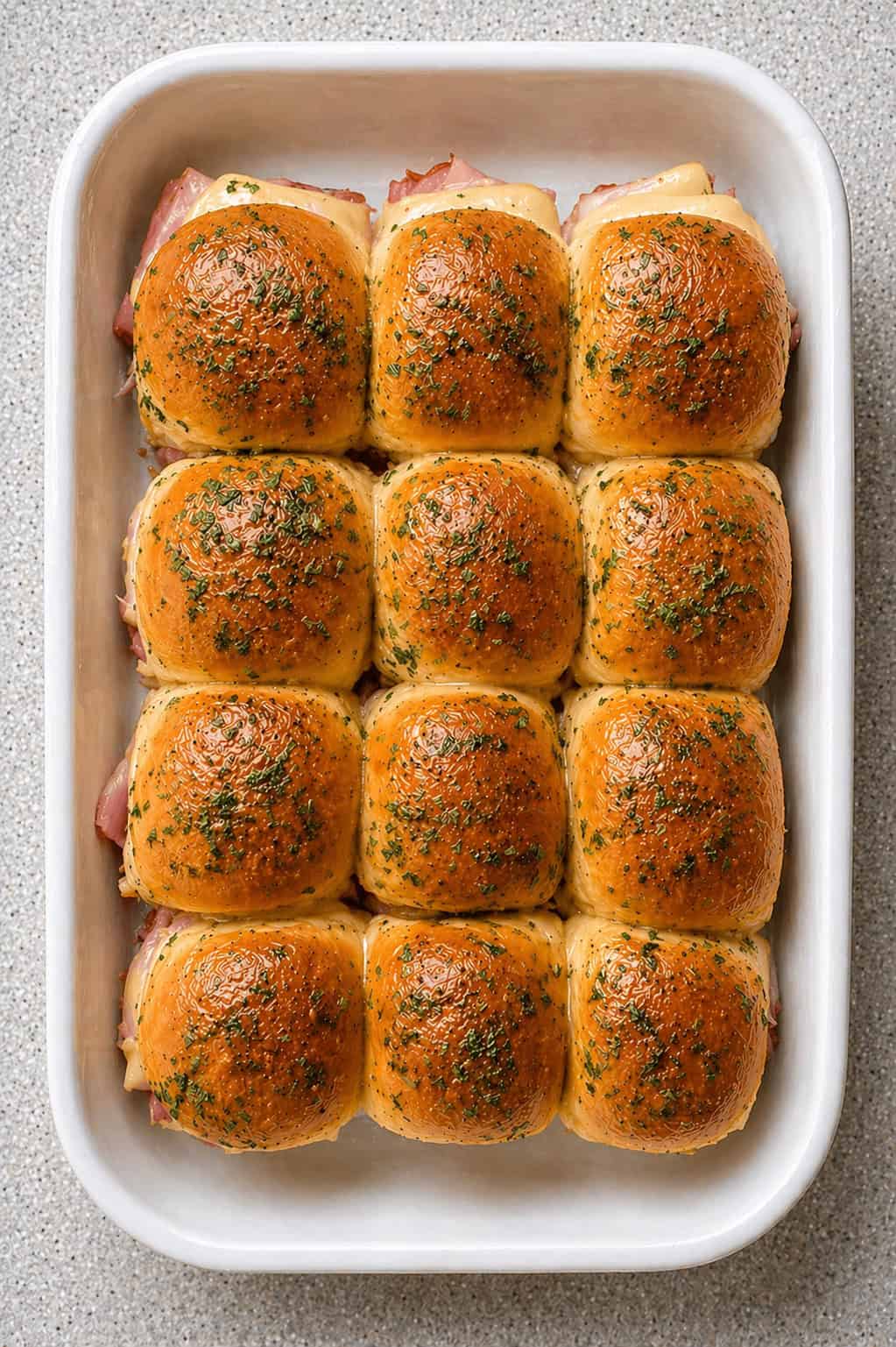 Ham and Swiss Sliders - layered in a white baking dish, filled with sliced ham and sliced swiss cheese.