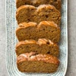 Five slices of Pumpkin Banana Bread are arranged in a row on a rectangular white plate with blue dotted patterns, placed on a light gray surface.