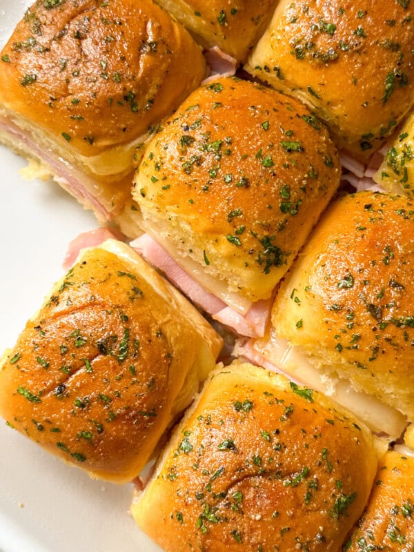 A group of baked ham and swiss hawaiian roll sliders with herb-topped golden brown buns.