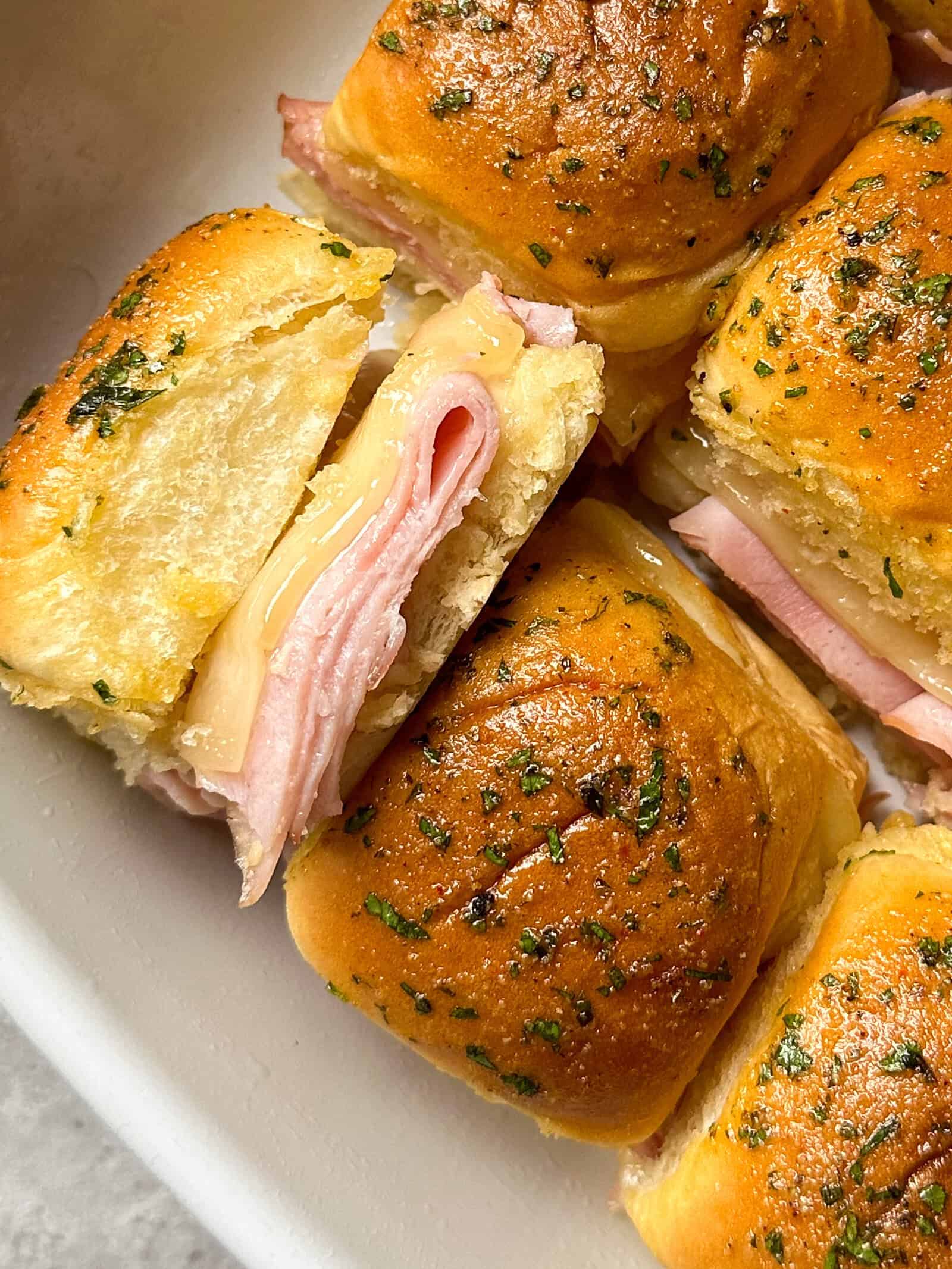 A pan of baked ham and swiss hawaiian roll sliders on small buns topped with herbs.