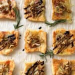 Square puff pastry bites topped with brie, walnuts, and rosemary make elegant Puff Pastry Appetizers. Arranged on parchment, some are drizzled with balsamic glaze and garnished with fresh rosemary for perfect Holiday Appetizers.
