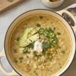 A pot of creamy white chicken chili, made from the best white chicken chili recipe, garnished with avocado, jalapeño, cilantro, and sour cream, served alongside tortilla chips and lime wedges.