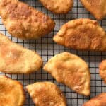 Golden brown panzerotti, reminiscent of mini calzones, are cooling on a black wire rack. The pastries are evenly spaced and display a crispy, flaky texture against a plain, light background.