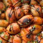 Close-up of a stuffed onions recipe topped with a balsamic glaze and garnished with chopped green herbs. The dish appears vibrant with a rich blend of colors and textures.