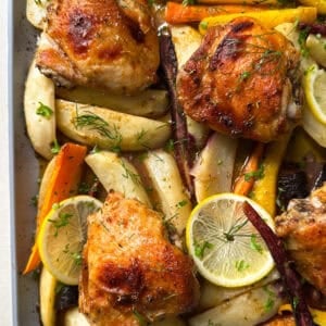 Golden roasted chicken thighs on a baking tray with colorful carrots, parsnips, potato wedges, lemon slices, and fresh herbs. This Sheet Pan Chicken and Potatoes recipe delivers tender veggies and perfectly caramelized flavors.