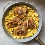 A skillet filled with creamy shell pasta topped with four pieces of seasoned, sliced chicken breast, garnished with chopped herbs and grated cheese.