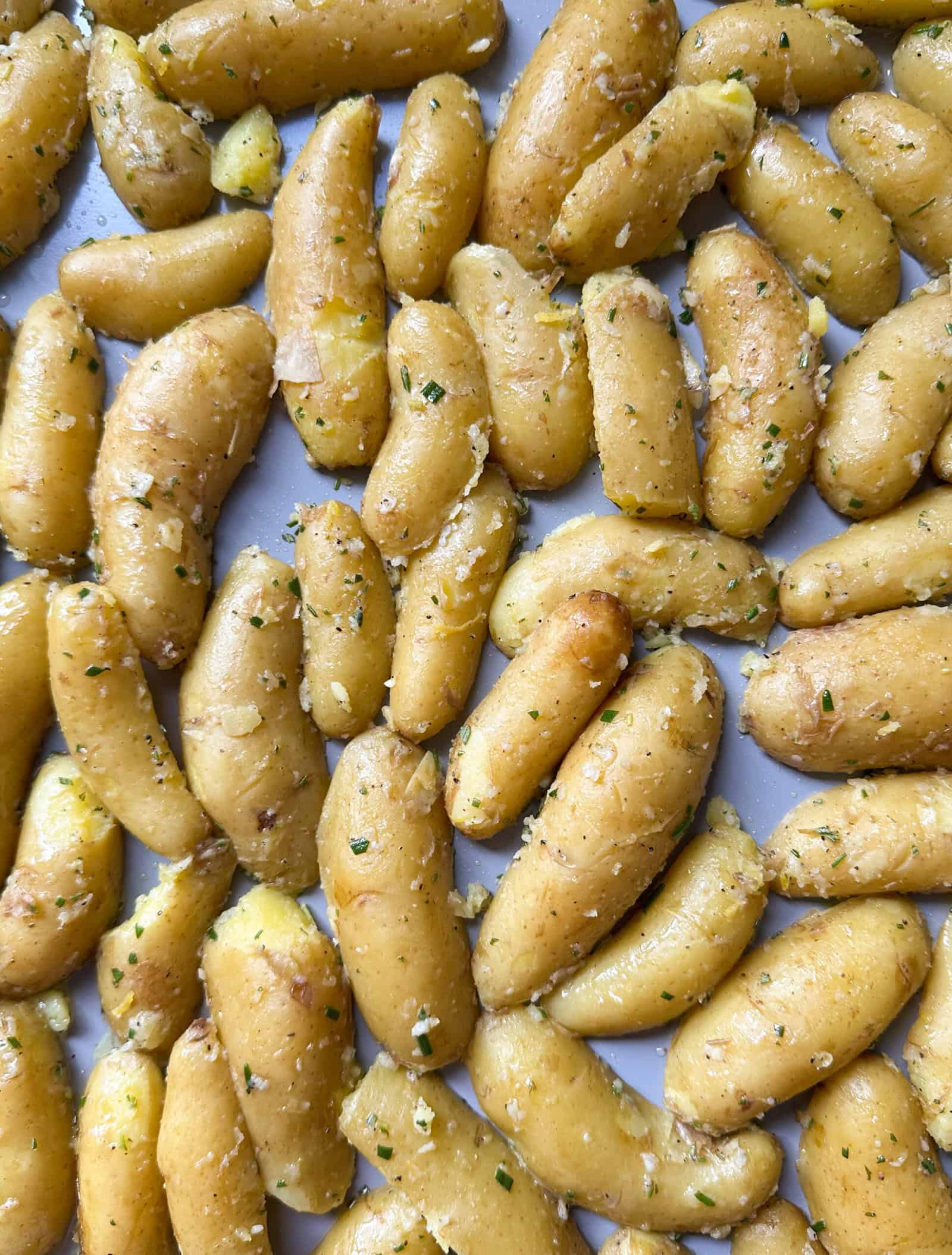 Close-up of roasted potatoes seasoned with herbs and spices, spread out on a baking sheet. The potatoes have a golden brown color and a slightly crispy texture—perfect for anyone seeking a delicious crispy roasted potatoes recipe.