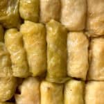 Close-up of several beginner-friendly cabbage rolls tightly packed together, with glossy, light green and yellowish cabbage leaves wrapped around the filling.