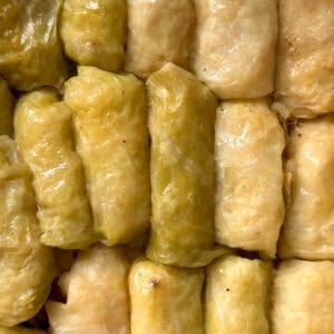 Close-up of several beginner-friendly cabbage rolls tightly packed together, with glossy, light green and yellowish cabbage leaves wrapped around the filling.