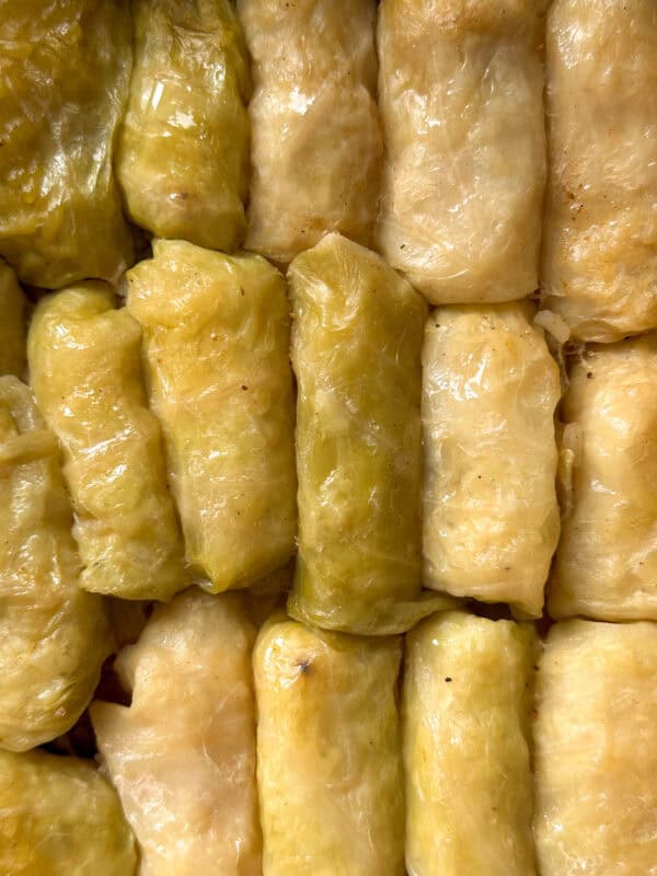 Close-up of several beginner-friendly cabbage rolls tightly packed together, with glossy, light green and yellowish cabbage leaves wrapped around the filling.