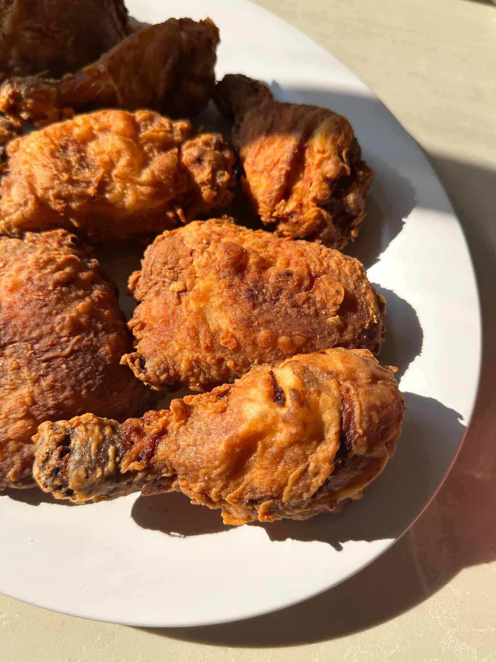 A close-up of crispy fried chicken drumsticks and thighs arranged on a white plate, with sunlight highlighting the golden brown crust—perfect inspiration for your next Crispy Fried Chicken Recipe.