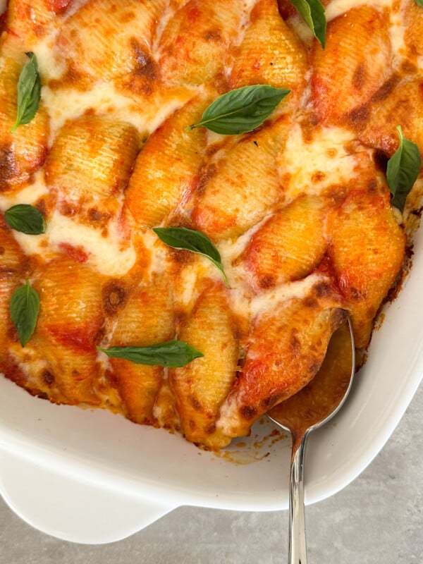 Baked stuffed pasta shells with ricotta, covered in melted cheese and tomato sauce, garnished with fresh basil leaves in a white baking dish with a serving spoon—the perfect stuffed pasta shells recipe.