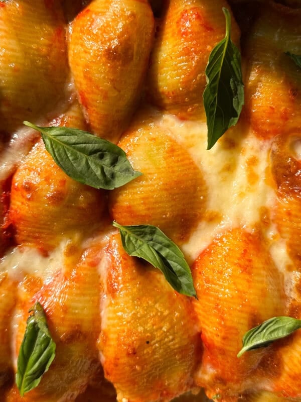 Close-up of baked stuffed pasta shells with ricotta, topped with melted cheese, tomato sauce, and fresh basil leaves.