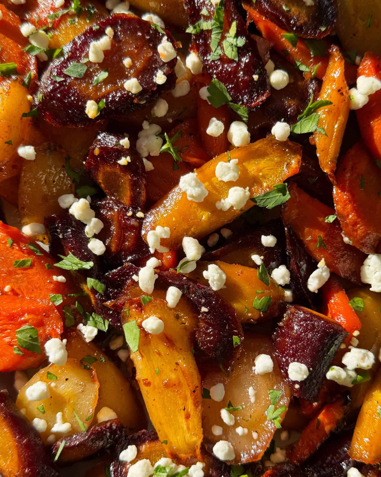 A close-up of Honey Glazed Carrots, topped with crumbled white cheese and sprinkled with chopped fresh herbs. The golden, orange, and purple carrots glisten with seasoning, making this Honey Glazed Carrots Recipe truly irresistible.