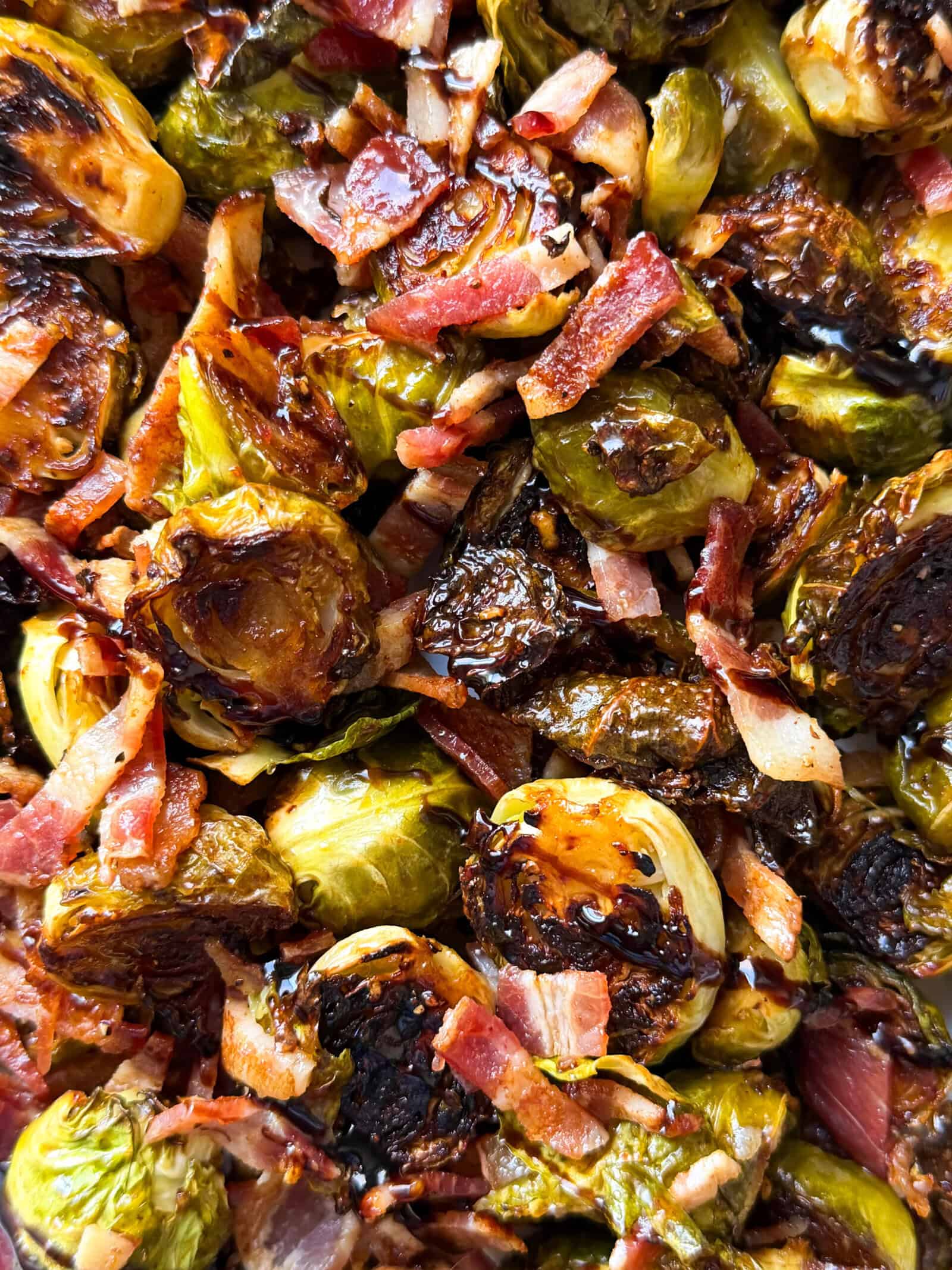 Close-up of roasted Brussels sprouts mixed with crispy bacon pieces, showing caramelized edges and a glossy, savory appearance—a delicious example of easy Roasted Brussels Sprouts Recipes.