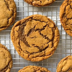 A close-up of several golden-brown Chewy Ginger Molasses Cookies with crackled tops cooling on a wire rack.