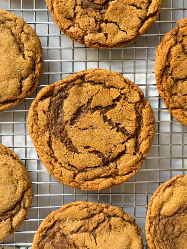 A close-up of several golden-brown Chewy Ginger Molasses Cookies with crackled tops cooling on a wire rack.