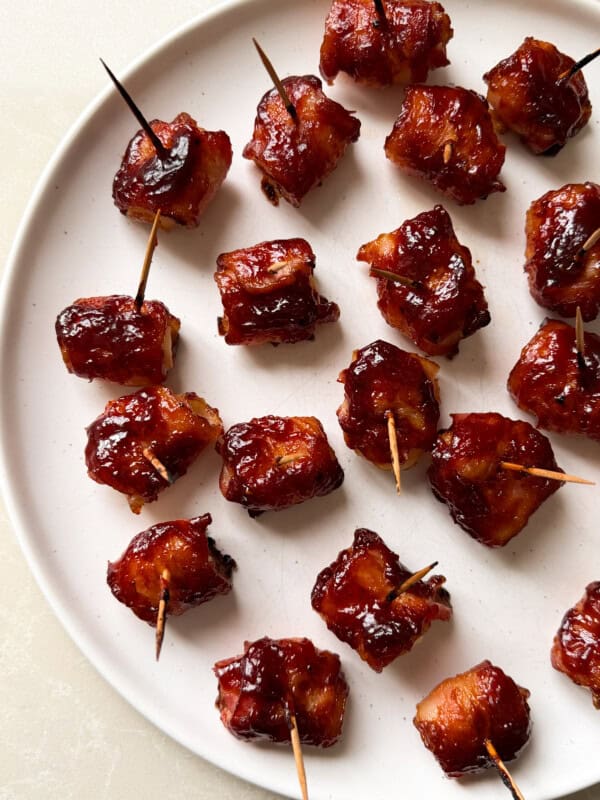 A white plate with several bacon wrapped water chestnuts secured with toothpicks, glazed with a shiny, dark sauce and arranged in an irregular pattern.