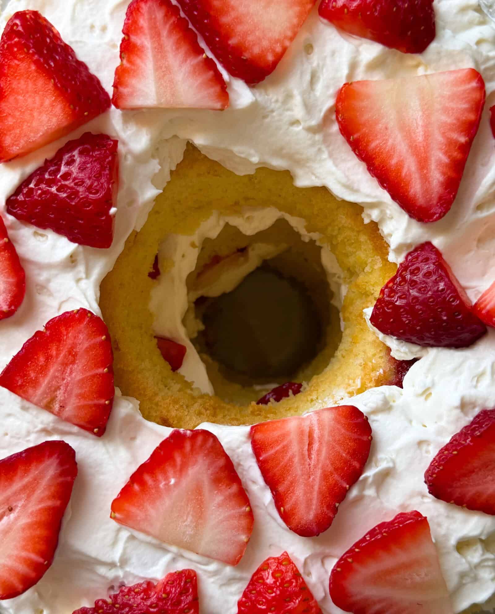 A close-up of a chiffon cake topped with whipped cream and fresh sliced strawberries, with the hole in the center of the cake visible.
