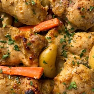 Close-up of maple mustard chicken pieces with golden-brown skin, baby potatoes, and carrot sticks, all garnished with chopped fresh parsley. A delectable sheet pan dinner idea that's well-seasoned and cooked to perfection.