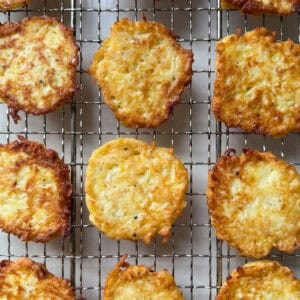 Golden brown potato latkes arranged in neat rows on a wire cooling rack, seen from above. Their crispy edges and textured surfaces showcase the irresistible appeal of a classic Potato Pancakes Recipe.