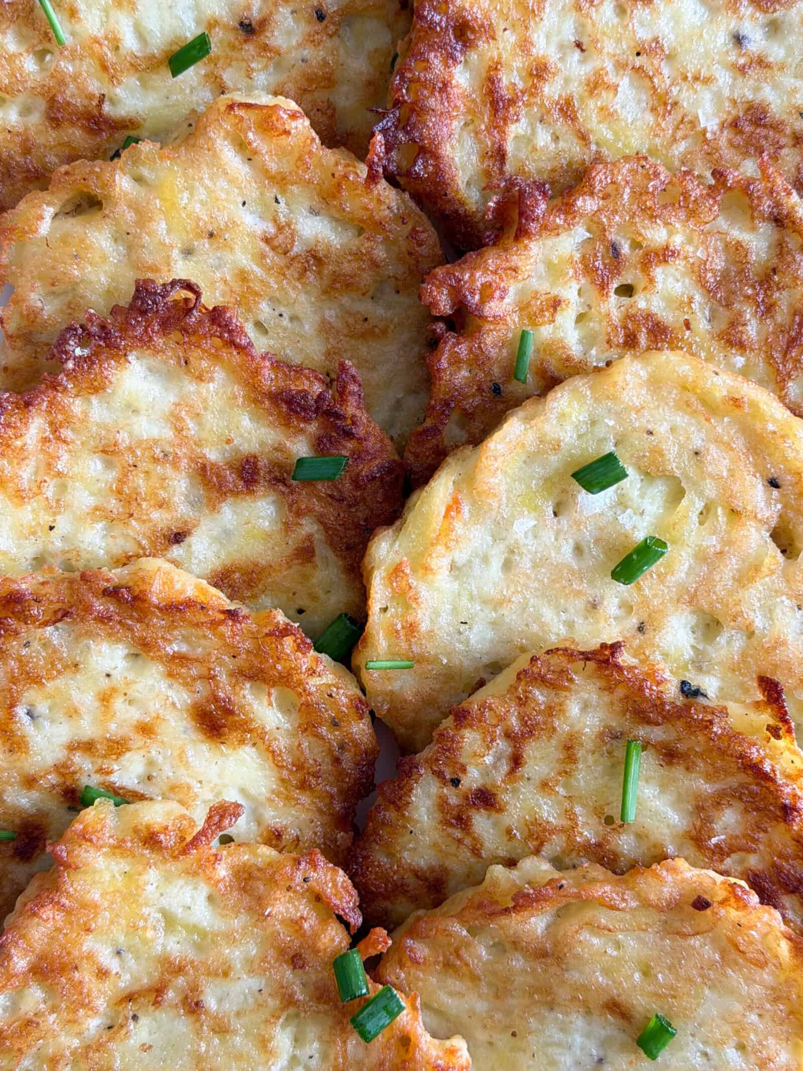 Golden brown German Potato Pancakes arranged closely together, garnished with a few pieces of chopped green chives. The pancakes have a crispy, textured surface.