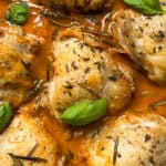 Golden-brown chicken thighs in a rich, orange-colored sauce with onions, garnished with fresh basil leaves, rosemary, and thyme. This savory chicken and onions recipe is perfect for delicious chicken dinners.