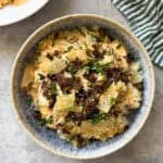A bowl of rice topped with ground beef, chopped chives, sesame seeds, diced yellow vegetables, and a creamy sauce brings Big Mac salad vibes—perfect if you love Big Mac cabbage and crispy rice bowls. Set on a light gray surface with a green striped cloth nearby.