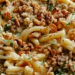 Close-up of creamy pasta mixed with ground meat, chopped walnuts, and garnished with fresh parsley.