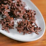 Clusters of chocolate-covered crispy chow mein noodles are arranged on a white oval plate, set on a wooden surface—an irresistible take on easy no bake desserts.