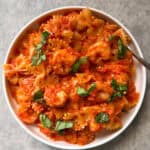A white bowl filled with Bowtie Pasta with Shrimp & Creamy Rosè, garnished with chopped fresh basil in a velvety rose sauce, sits on a light gray surface.